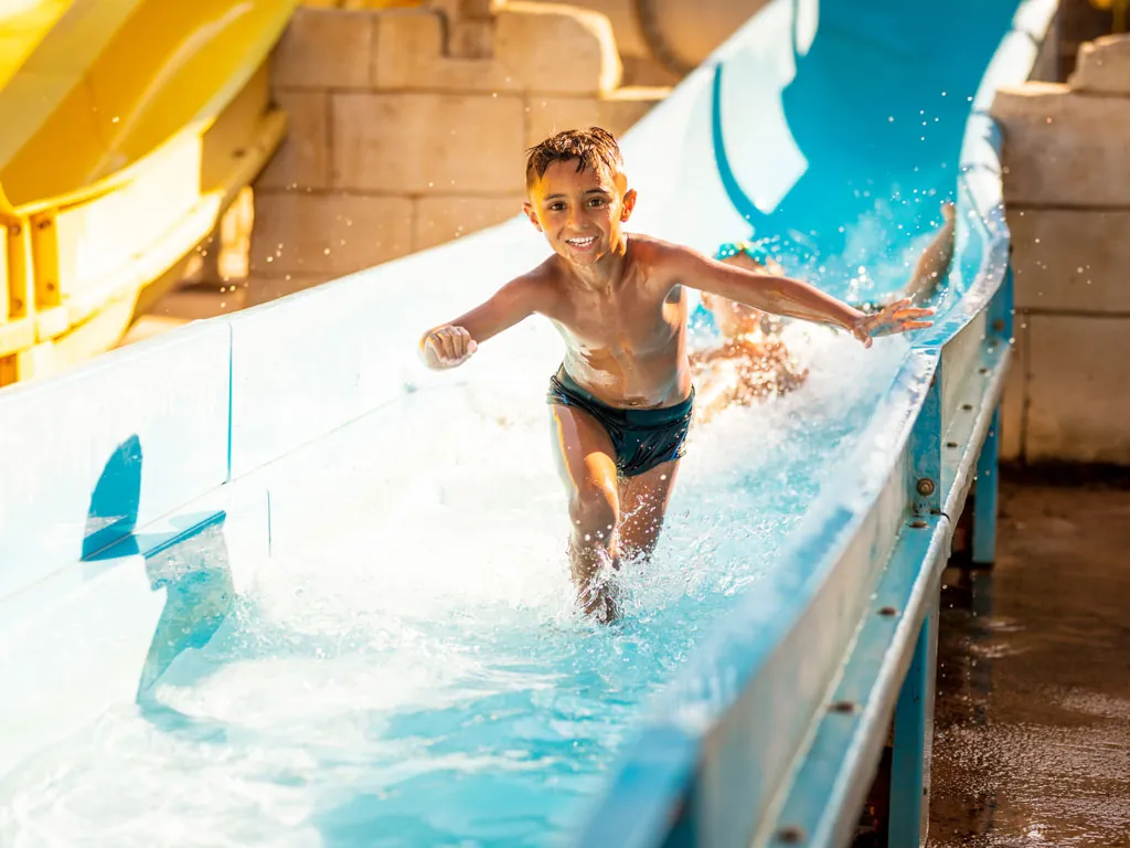 enfant qui sort du toboggan aquatique de l'espace piscine du camping hadotel Le Trivoly à Torreilles Plages - Pyrénées Orientales